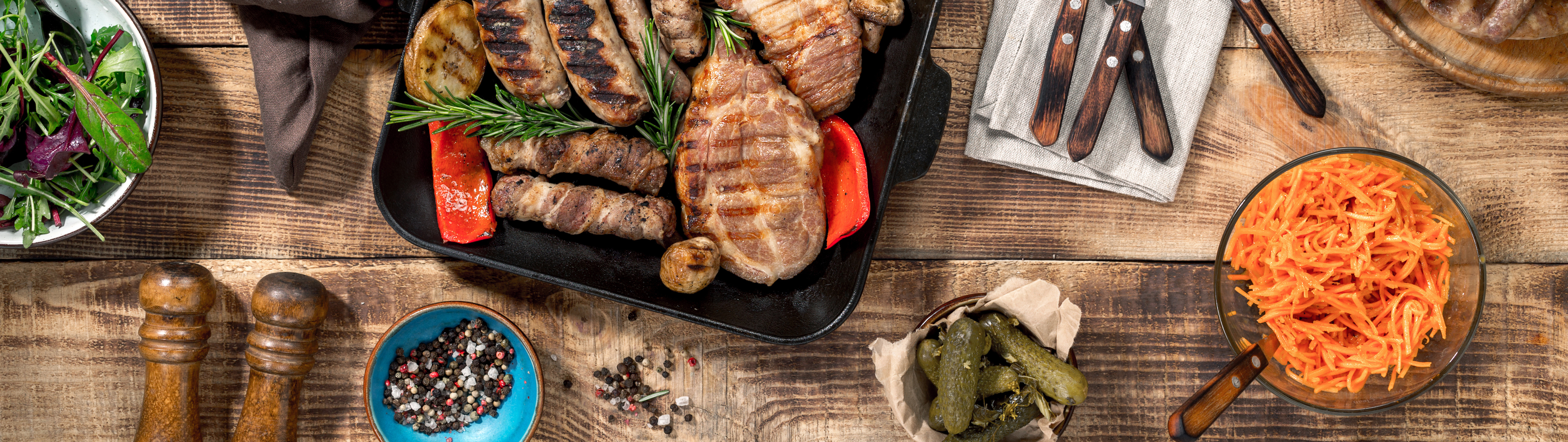 On a wooden table different food cooked on the grill. Grilled steak, grilled sausages, grilled vegetables on the wooden table, top view
